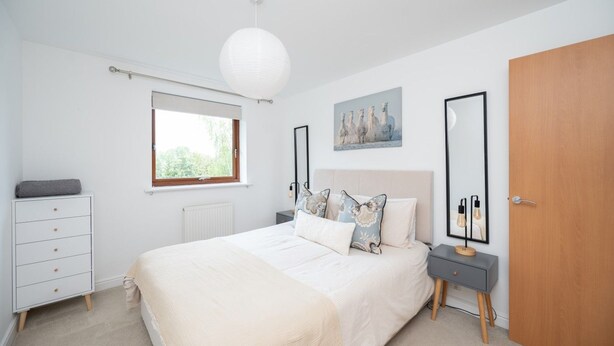 A bedroom with a bed, a dresser, a window, a door, and a wall-mounted mirror. - 2 Bedroom Flat Free Parking Close to Gatwick (West Sussex)