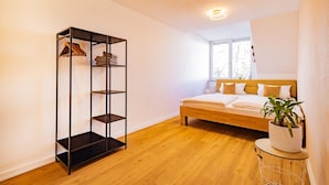 A bedroom with a bed, a wooden floor, a metal shelving unit, and a potted plant. - Apartment 'Kim Fewo 4' with Wi-Fi (Emmendingen)