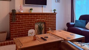 Un saló amb una llar de pedra, un televisor de pantalla plana muntat a la part superior, un sofà de cuir i una taula de centre de fusta.