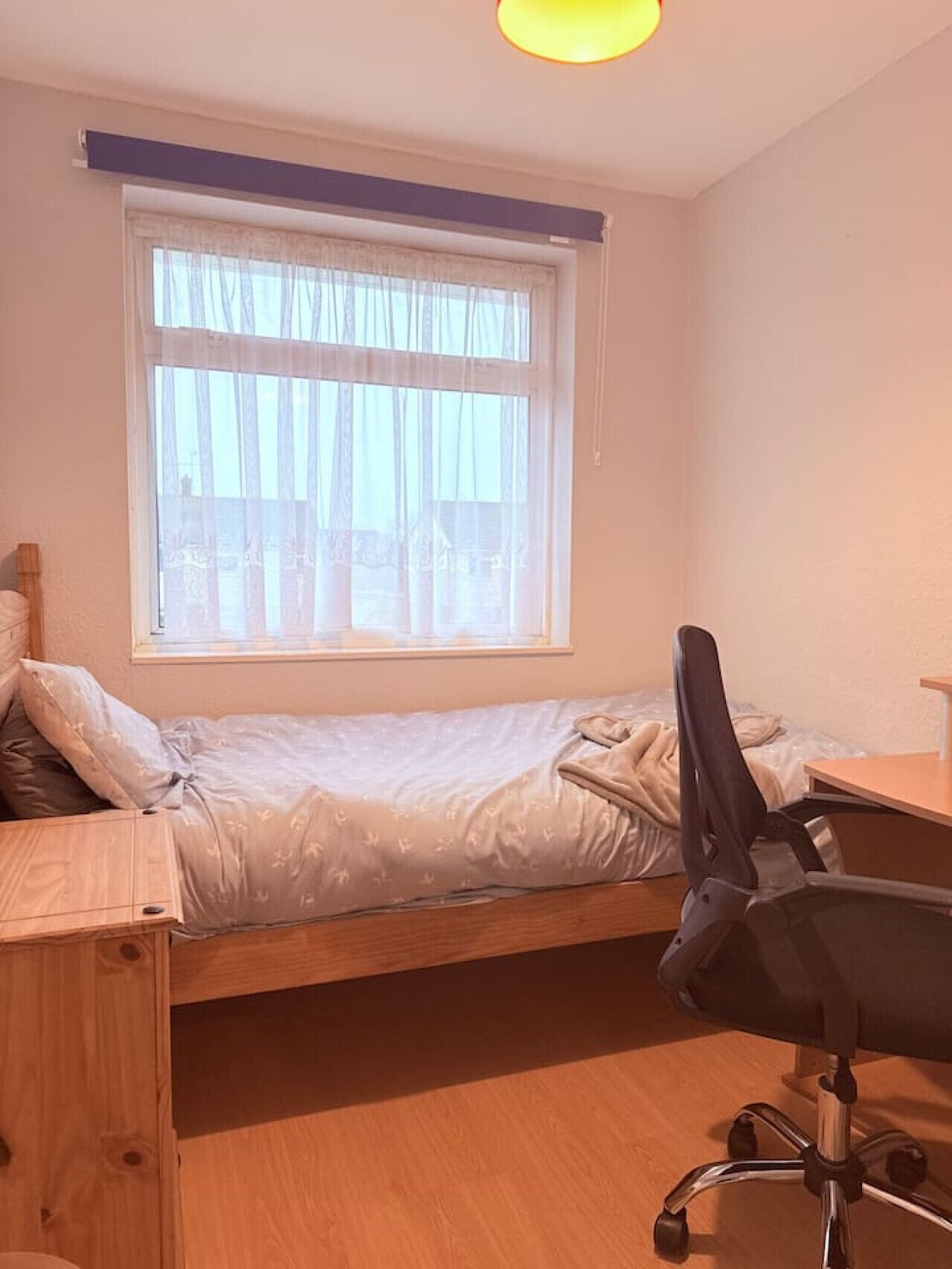 Un dormitorio pequeño y ordenado con una cama individual, un escritorio y una silla.