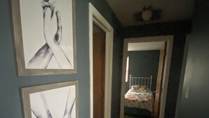 Um corredor com duas obras de arte emolduradas na parede, uma porta que dá para um quarto e uma cama com colcha florida.