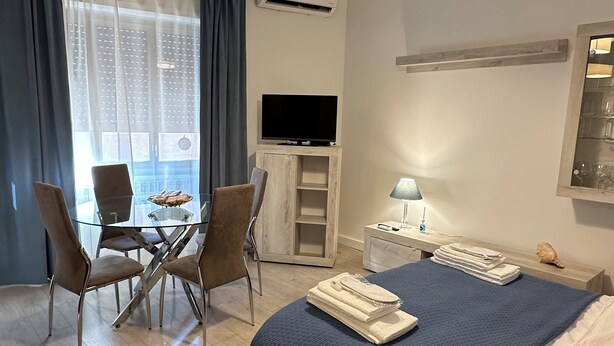 A hotel room with a bed, a desk with a chair, a TV, and a window with curtains. - Vatican YH (Roma)