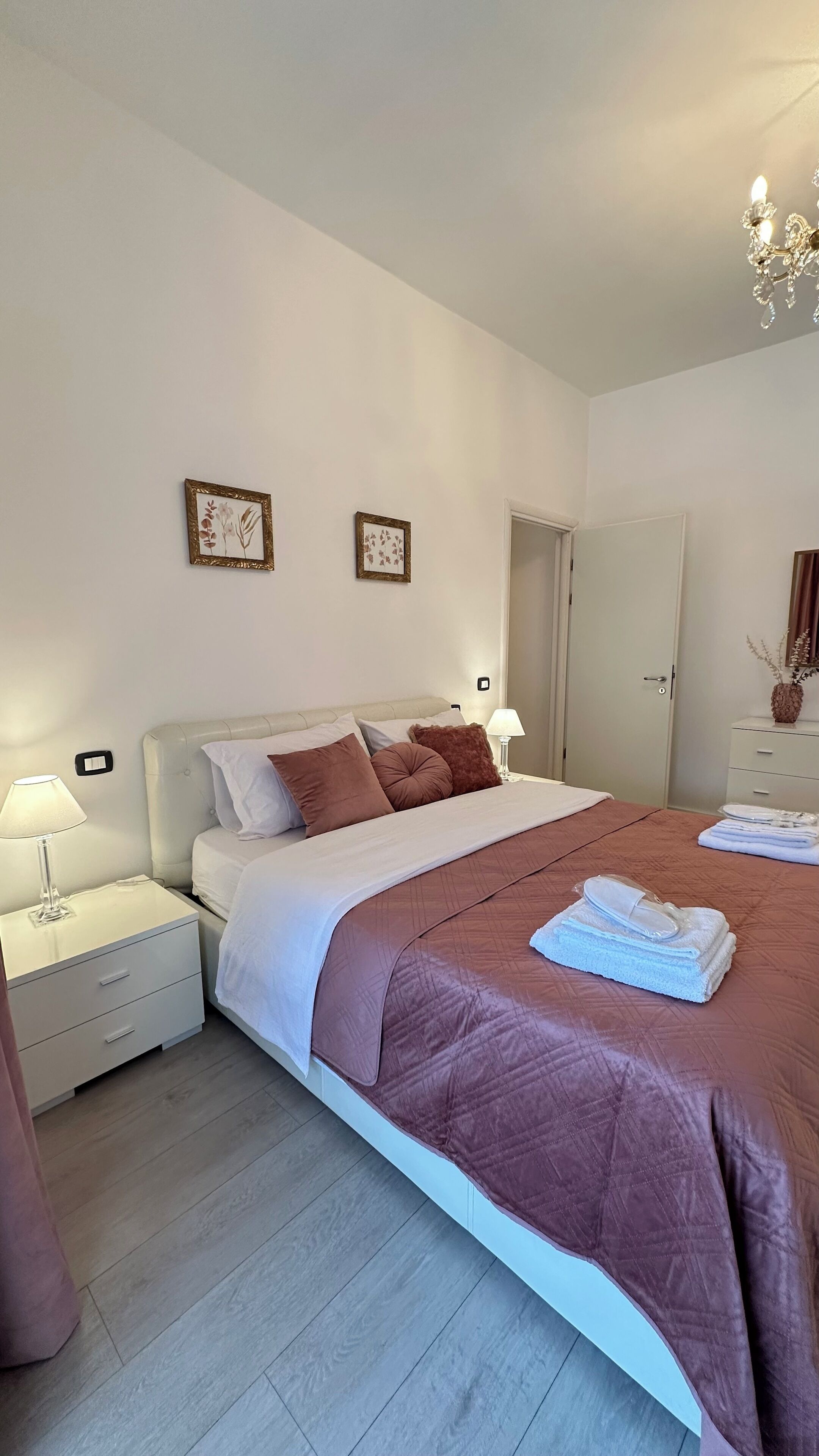 Une chambre à coucher bien rangée, avec un lit, des tables de chevet, une commode, une lampe et une porte.