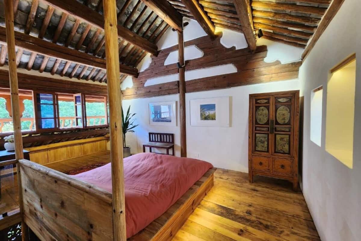 A room with a wooden four-poster bed, a wooden cabinet with clocks, and a bench.
