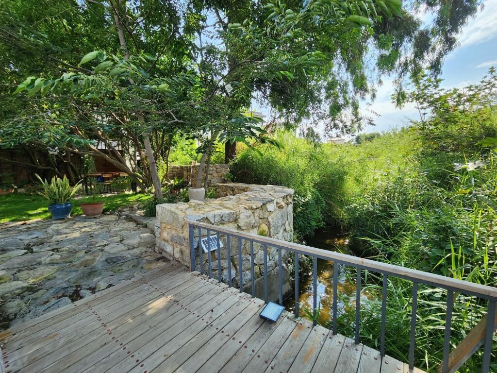 Eine Holzterrasse mit einer Steinsäule und einem Metallgeländer, das auf einen Garten mit einem kleinen Bach blickt.