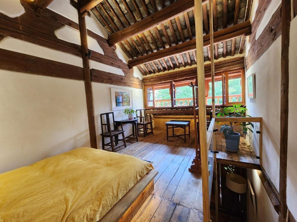 Ein rustikales Zimmer mit einem hölzernen Bett, einem Schreibtisch mit Stühlen und einem Fenster mit Blick auf Grünfläche.