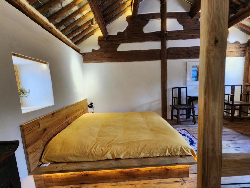 A bedroom with a wooden bed, a sloped ceiling, and a small table with chairs.