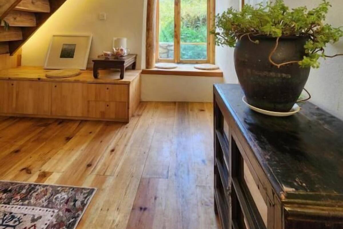 A wooden staircase leading to a loft bedroom with a large window, a potted plant, and a wooden bench.