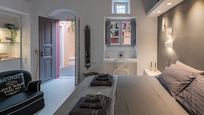 A modern bedroom with a bed, bedside tables, a desk, a chair, a wardrobe, and a window with plants. - Coat Of Arms Mansion (Santorini)