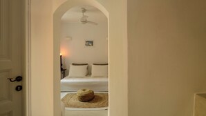 A hallway leading to a bedroom with a bed, a ceiling fan, and a small picture on the wall. - Coat Of Arms Mansion (Santorini)