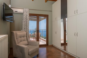 A room with a sofa, a TV mounted on the wall, a sliding glass door leading to a balcony with a view, and a white wardrobe. - Villa 'Zante Oliva Blu-Seaview With' with Sea View, Wi-Fi & Air Conditioning (Zakynthos Town)