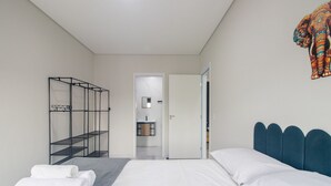 Ein modernes Hotelzimmer mit einem Bett, einem Metallschrank, einem durchgehenden Türspalt erkennbaren Badezimmer und einer farbenfrohen Wanddekoration.