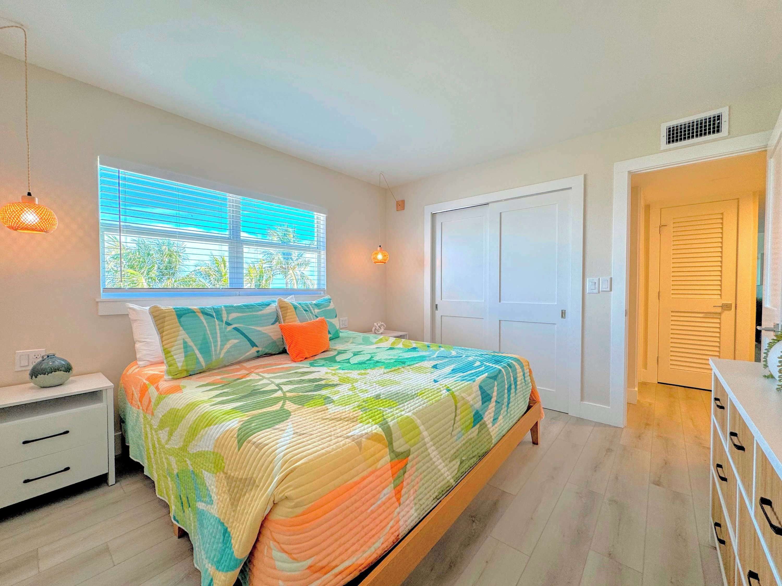 Ein Schlafzimmer mit Bett, Fenster, Nachttisch, Kommode und Tür.