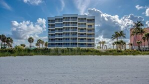 A multi-story hotel with a modern design, located on a beach with palm trees and a clear sky. - Vacation Villas #431 Stunning Beachfront Condo (Fort Myers Beach)