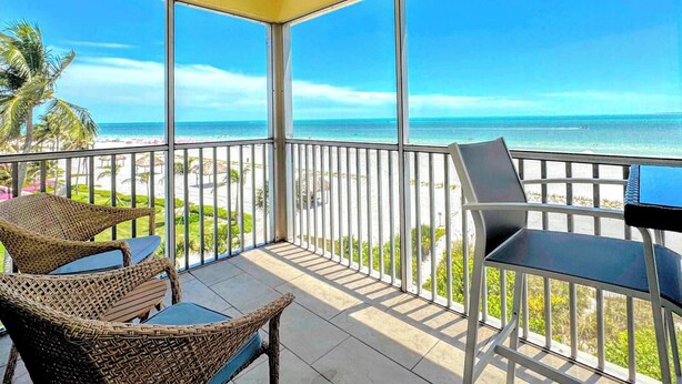 A balcony with wicker chairs, a table, and a view of the beach and ocean. - Vacation Villas #431 Stunning Beachfront Condo (Fort Myers Beach)