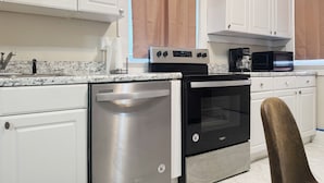 Una cocina moderna con armarios blancos, un lavavajillas de acero inoxidable, un horno negro y un microondas.