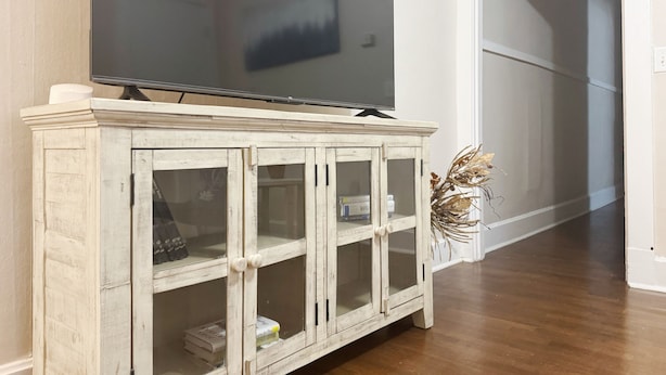 Un mueble de madera con puertas de cristal, un televisor de pantalla plana encima y una planta decorativa a su lado.