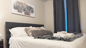 Una cama bien hecha con ropa blanca, un cabecero oscuro y una manta gris.
