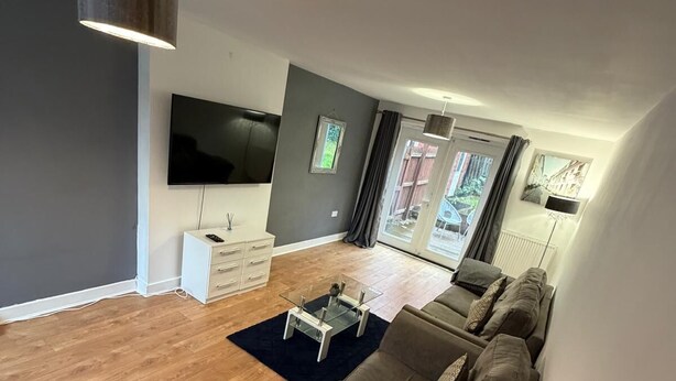 Una sala de estar moderna con un sofá grande de color gris, un televisor de pantalla plana montado en la pared y piso de madera.