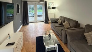 Una sala de estar moderna con un sofá, una mesa de centro y un televisor. Hay una puerta corrediza de vidrio que da a un espacio exterior.