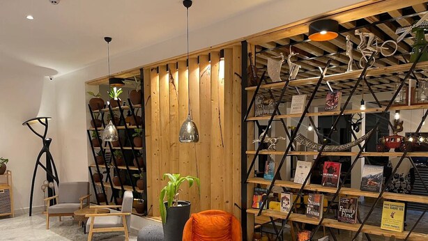 Ein modernes Wohnzimmer mit einem Bücherregal aus Holz, einem runden Holztisch und einer großen Topfpflanze.