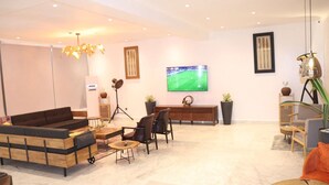 Ein modernes Wohnzimmer mit einer Couch, Sesseln, einem Couchtisch und einem Fernseher an der Wand.