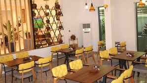 Ein Restaurant mit gelb gepolsterten Stühlen und Holztischen, einer Holzwand mit Blumentöpfen und hängenden Pendelleuchten.