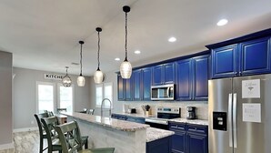 Een moderne keuken met blauwe kastjes, roestvrijstalen apparatuur en een marmeren kookeiland.