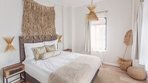 A bedroom with a large bed, a woven headboard, a hanging light fixture, and a window with curtains.