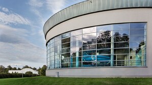 A modern building with a curved facade and large windows reflecting the sky and trees.