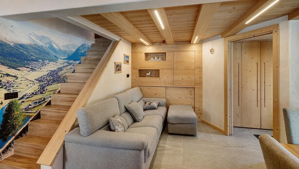 A modern living room with a wooden staircase, a sofa, and a mural of a mountainous landscape. - Apartment 'Alpino' with Balcony and Wi-Fi (Livigno)