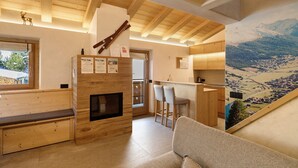 A wooden interior with a fireplace, seating area, and a view of a mountainous landscape. - Apartment 'Alpino' with Balcony and Wi-Fi (Livigno)