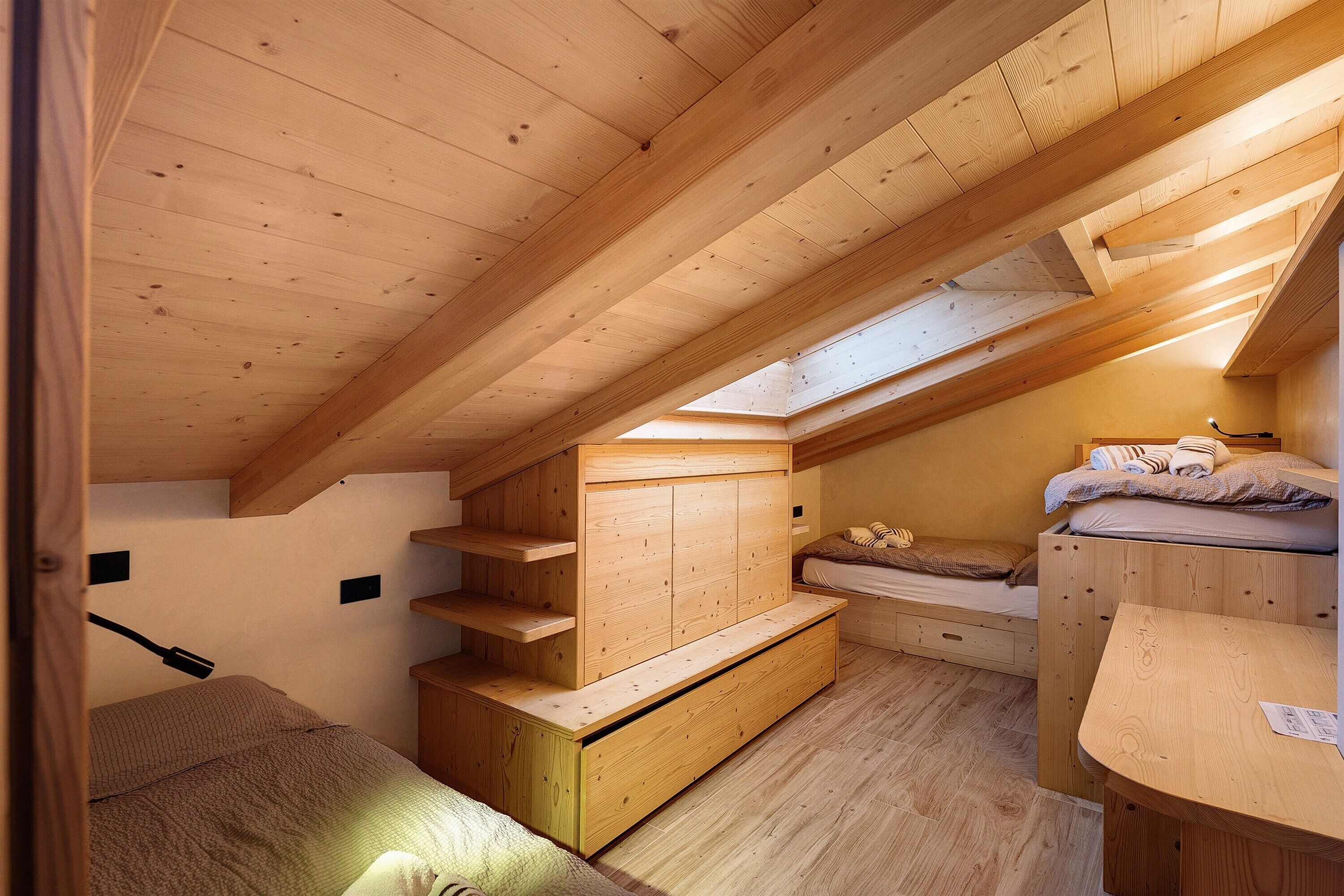 A compact room with a sloped ceiling, built-in wooden shelves, a bed, and a small desk.