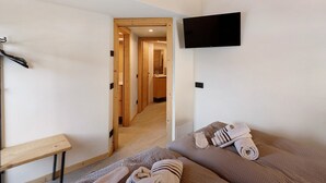 A hotel room with a bed, a TV mounted on the wall, a wooden table, and a hallway leading to a bathroom. - Apartment 'Alpino' with Balcony and Wi-Fi (Livigno)