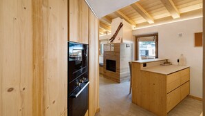 A wooden interior with a kitchen area, wooden cabinets, a fireplace, and a window. - Apartment 'Alpino' with Balcony and Wi-Fi (Livigno)