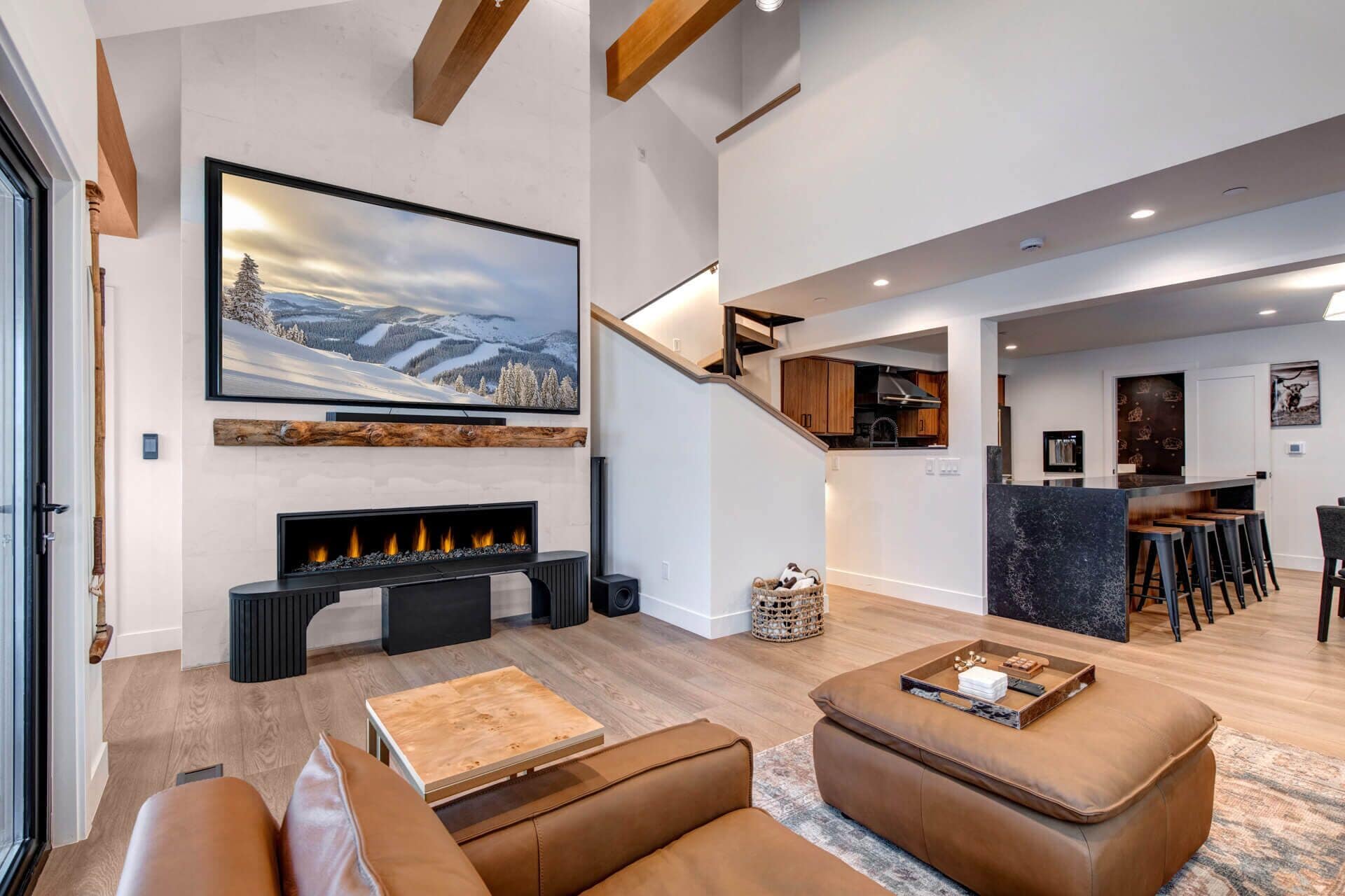 Una sala de estar moderna con chimenea, sofás de cuero, una mesa de centro de madera y un televisor grande montado en la pared.