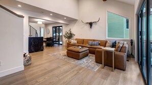 A spacious living room with a large brown leather sofa, a coffee table, and a dining area with a table and chairs. A bull's head mounted on the wall adds a unique decor element. - Moose Mgmt at Upper Main 301 (Park City)
