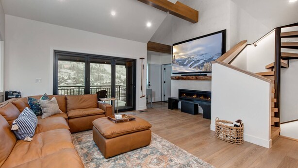 A spacious living room with a large sofa, a fireplace, and a view of a snowy mountain landscape. - Moose Mgmt at Upper Main 301 (Park City)