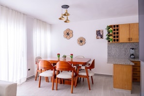 A dining area with a wooden table and chairs, a kitchen with granite countertops, and decorative wall art. - 3 BR Villa With Private Pool and Jacuzzi (Punta Cana)