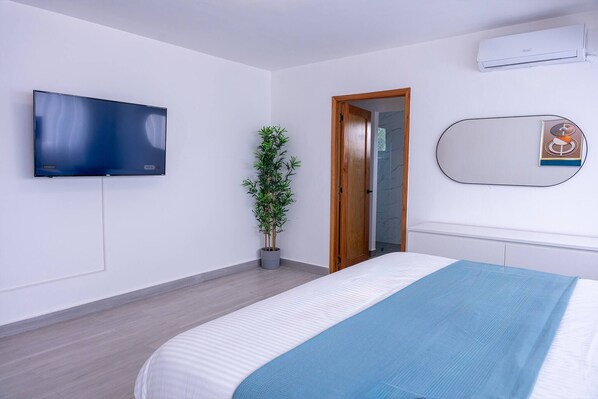 A modern bedroom with a flat-screen TV, a potted plant, a wooden door, and a bedside mirror. - 3 BR Villa With Private Pool and Jacuzzi (Punta Cana)