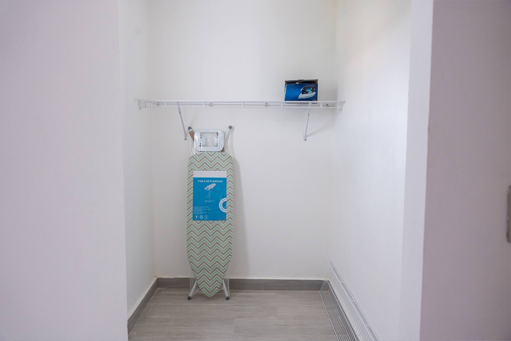 A small room with a wall-mounted ironing board and a shelf above it.