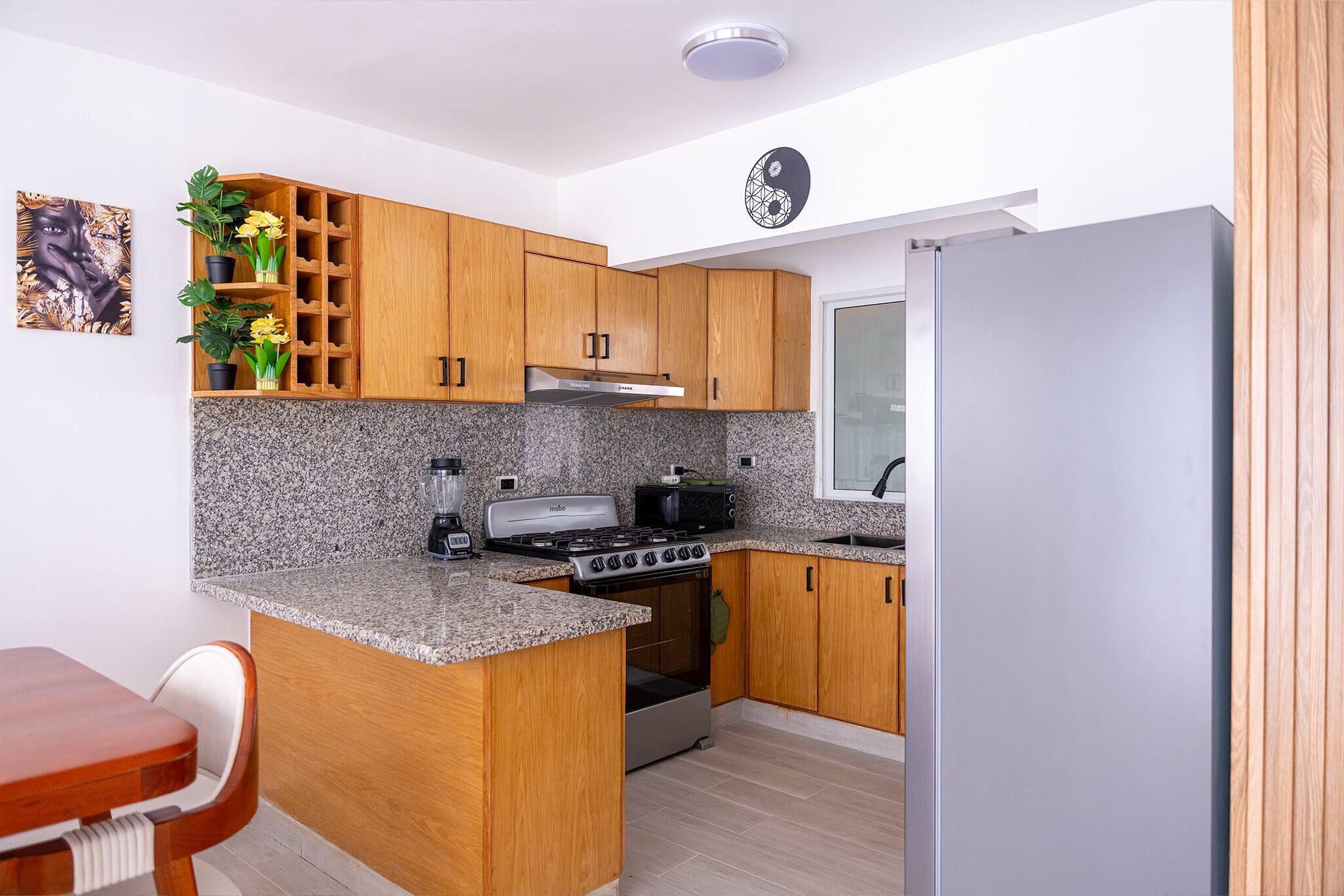 Una cucina moderna con piani in granito, mobili in legno, forno integrato, piano cottura e frigorifero.