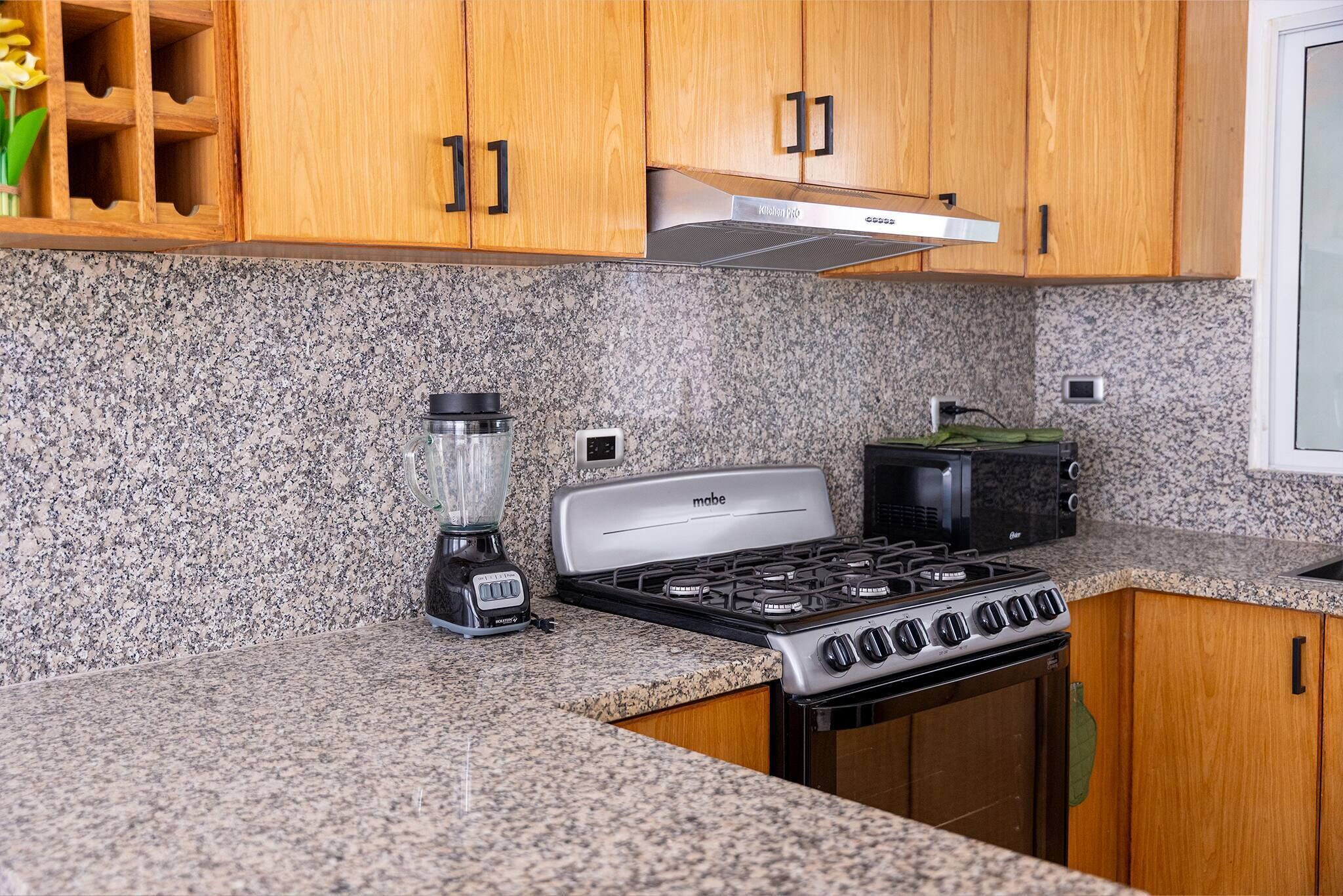 A kitchen with granite countertops, wooden cabinets, a gas stove, a microwave, and a blender.