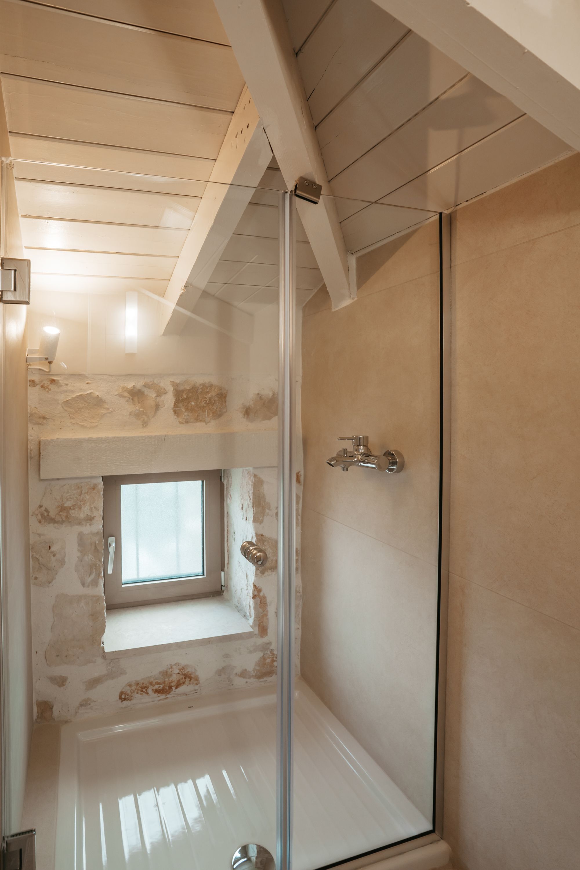 Eine Dusche mit Glastür, Fenster und Steinwand.
