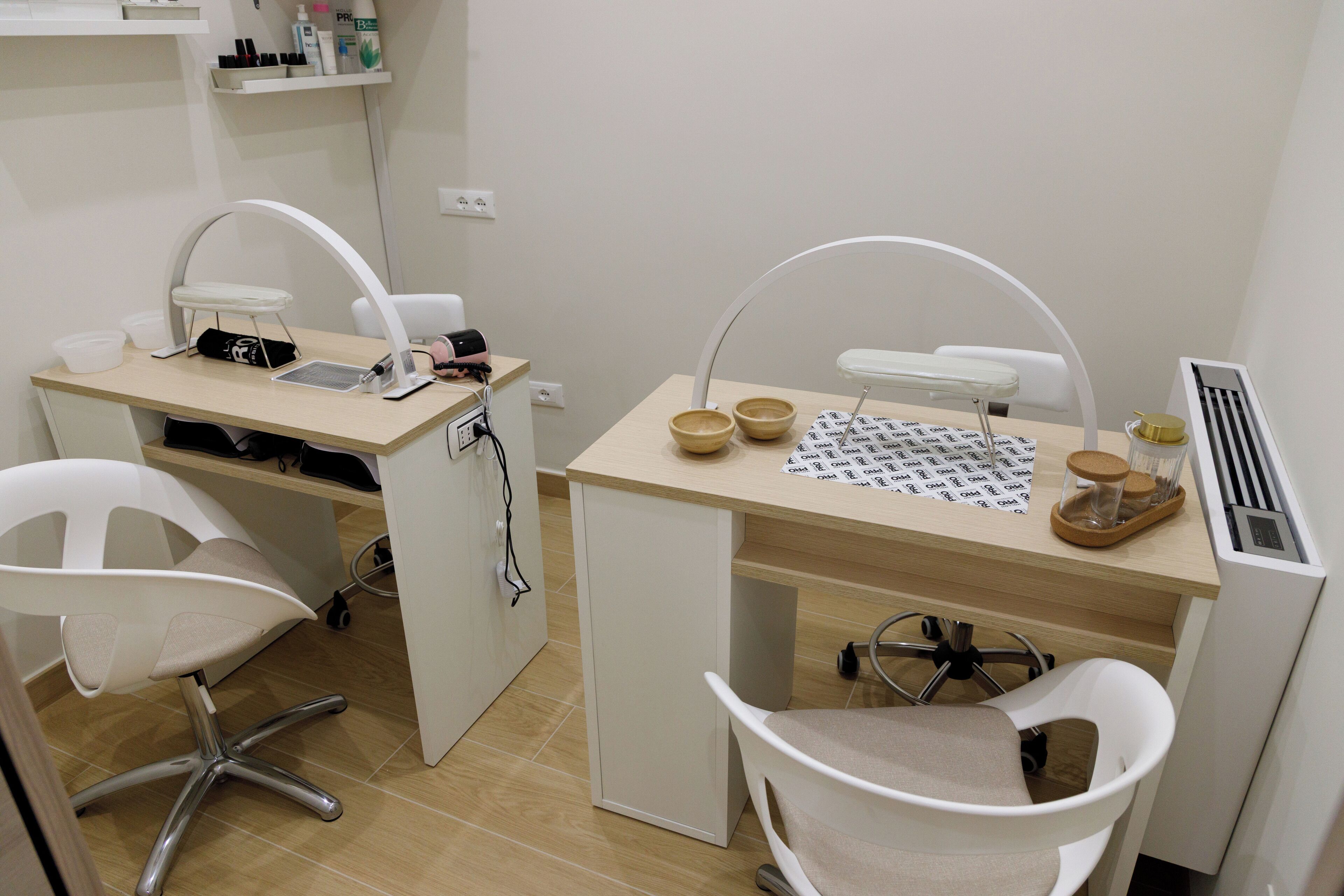 A small, clean room with two white chairs, a desk with a computer, and a shelf with toiletries.