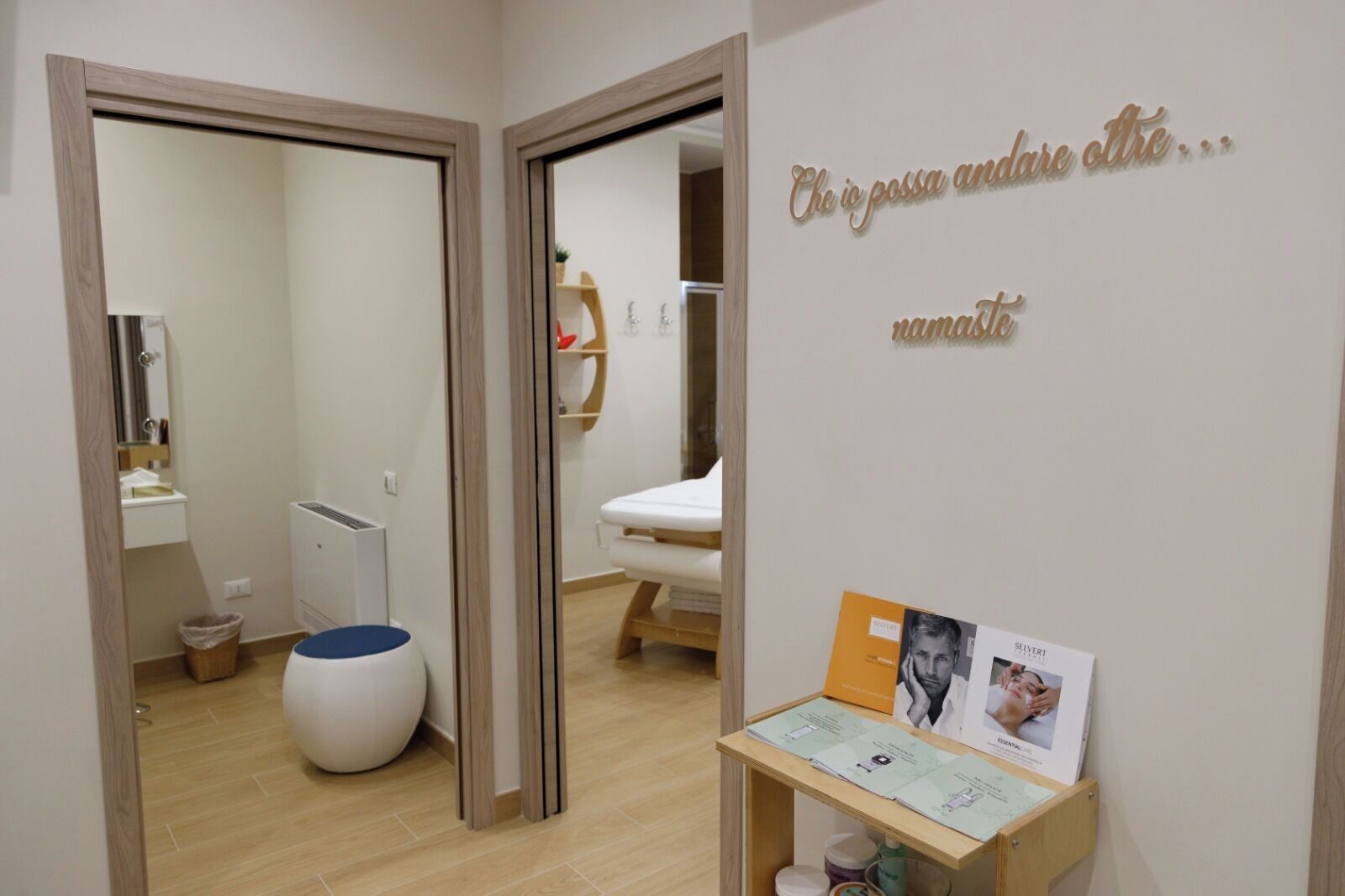 A bathroom with a toilet, bidet, and sink. There is a mirror, a towel rack, and a small shelf with toiletries.