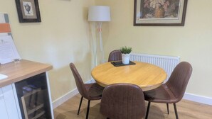 A dining area with a round wooden table, four brown chairs, a white radiator, and framed pictures on the wall. - The Tack Room With Hot Tub (Doncaster)