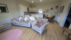 A cozy living room with two sofas, a pink rug, and a dining area with a table and chairs. - The Tack Room With Hot Tub (Doncaster)