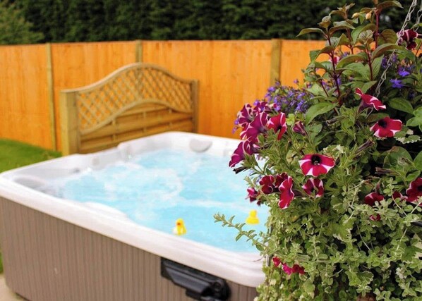 A hot tub with a wooden fence and a planter with flowers in the foreground. - The Stirrups Cottage With Hot Tub (Doncaster)