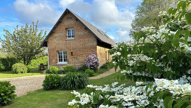 Un bâtiment en pierre doté d’un toit à deux versants, entouré de jardins bien entretenus et de plantes en fleurs.